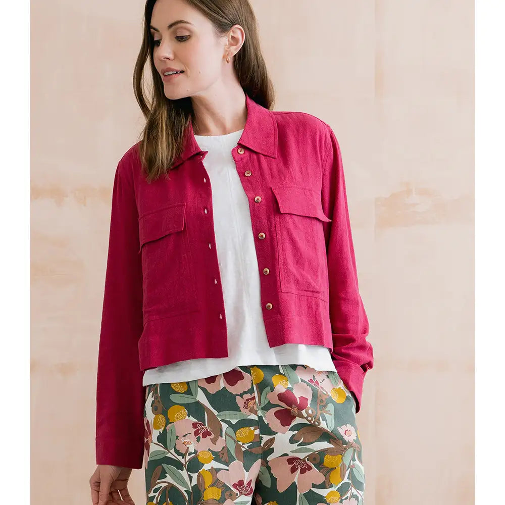 Woman wearing a red jacket over a white shirt with floral pants against a beige background