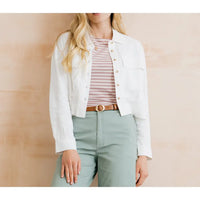Person wearing a white jacket over a striped shirt with light green pants against a beige background