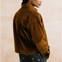 A woman wearing a brown corduroy jacket, shown from a side-back angle against a textured beige wall.
