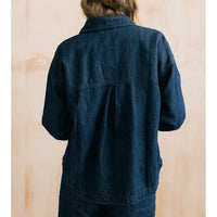 A person viewed from the back wearing a dark indigo denim jacket or overshirt against a light beige wall.
