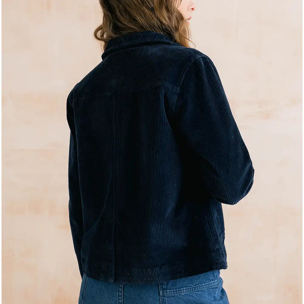 A person shown from the back wearing a dark navy corduroy jacket and blue jeans, standing against a light beige textured wall.