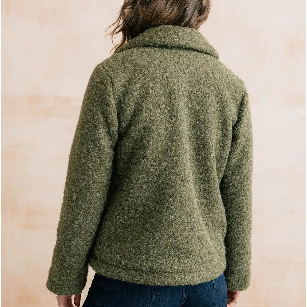 A person shown from the back wearing a textured, boucle-style olive green fleece jacket against a light beige background.