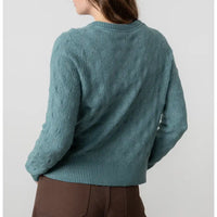 Teal cable knit sweater worn by a person on a light gray background