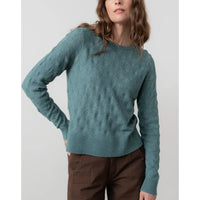 Woman wearing a teal sweater against a plain background