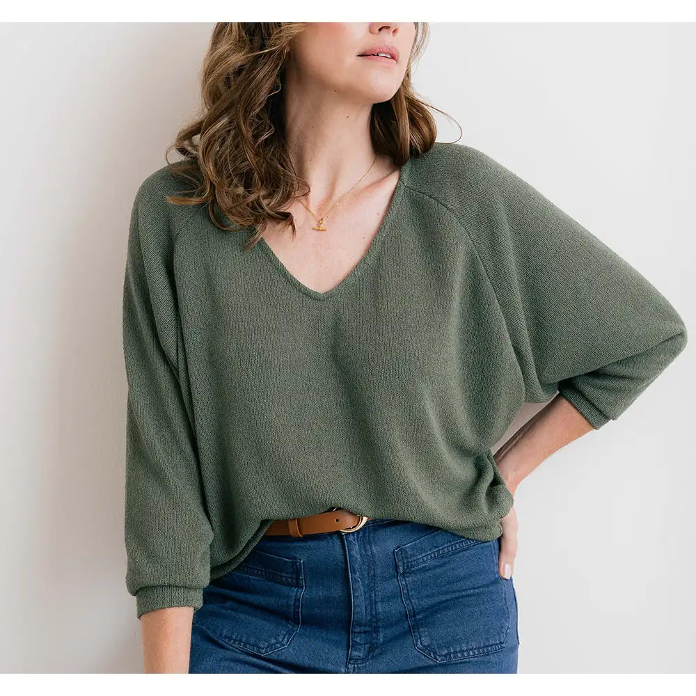 Woman wearing a green sweater and blue jeans against a white background