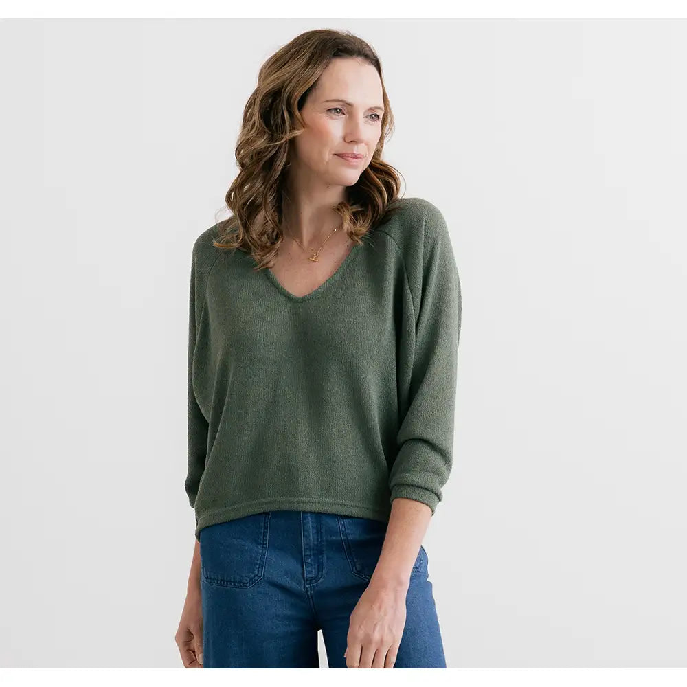 Woman wearing a green sweater and blue jeans on a white background