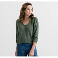 Woman wearing a green sweater and blue jeans on a white background