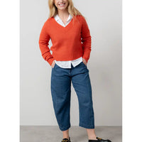 Person wearing an orange sweater, white shirt, and blue jeans against a plain background