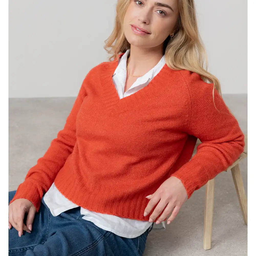 Woman wearing a red sweater over a white shirt, sitting on a chair.