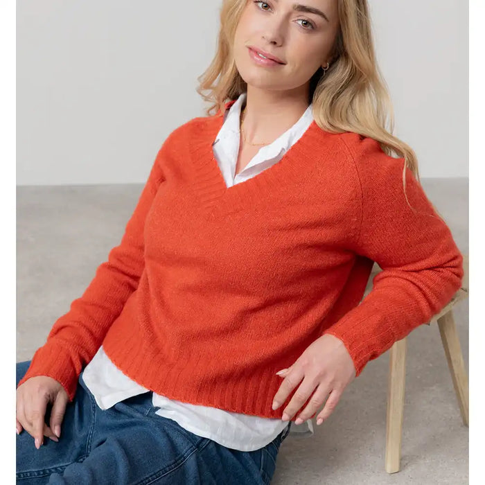 Woman wearing a red sweater over a white shirt, sitting on a chair.