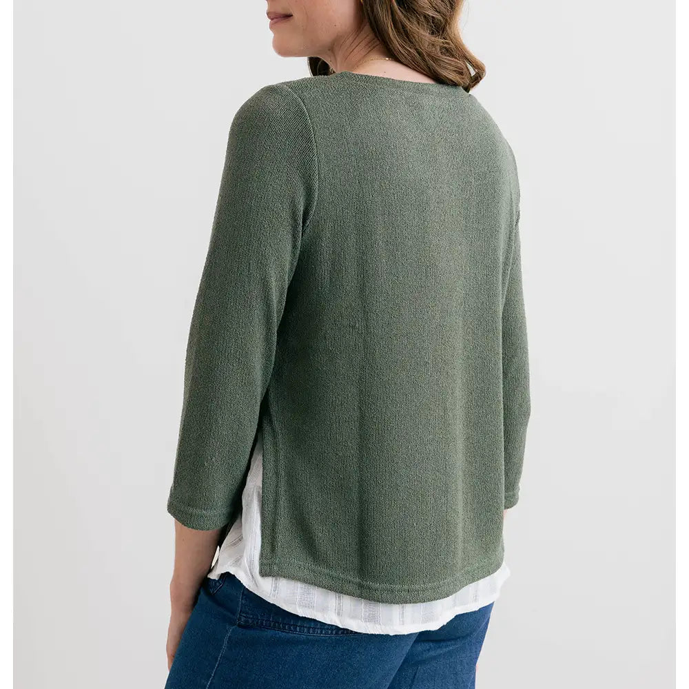 Person wearing a green long-sleeve shirt over a white top with blue pants on a light gray background