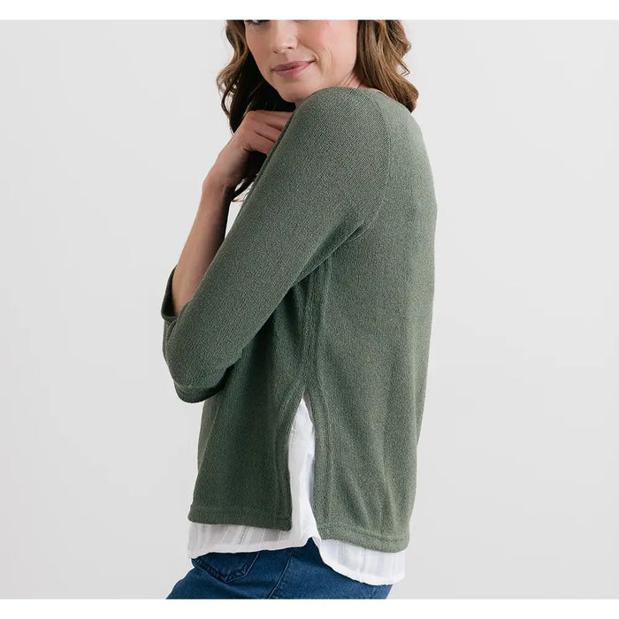 Woman wearing a green sweater over a white shirt on a plain background