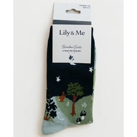 A pair of Lily & Me bamboo socks in a dark navy blue color, featuring a whimsical forest pattern with green trees, a brown rabbit, white stars, and a light blue-gray toe section. The socks are shown in their original retail packaging with a white paper header card.