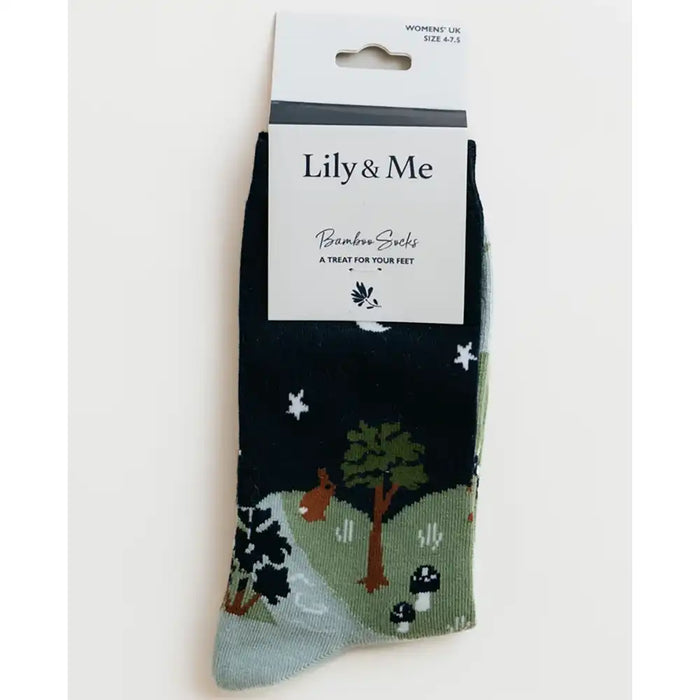 A pair of Lily & Me bamboo socks in a dark navy blue color, featuring a whimsical forest pattern with green trees, a brown rabbit, white stars, and a light blue-gray toe section. The socks are shown in their original retail packaging with a white paper header card.