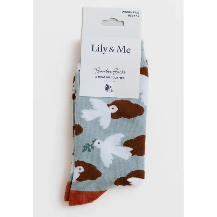 A pair of Lily & Me bamboo socks in a light blue-gray color, featuring a pattern of white doves and brown hedgehogs, with a white cardboard hanger packaging.
