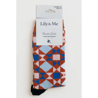 A pair of Lily & Me bamboo socks with a geometric diamond pattern in blue, rust orange, and light blue on a white background, packaged in a white cardboard sleeve.