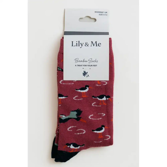 A pair of Lily & Me bamboo socks in a dusty rose color, featuring a pattern of black and white birds with orange beaks and white circular scratch marks. The socks are displayed on their white cardboard hanger packaging against a plain white background.