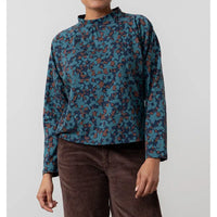 Person wearing a blue and brown patterned shirt with brown pants on a light gray background