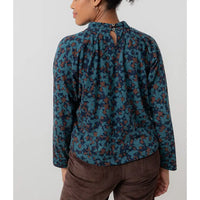 Person wearing a patterned teal and brown blouse with a plain background