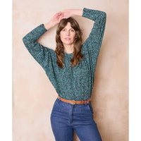 Woman wearing a green floral blouse and blue jeans against a beige background