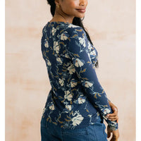 A woman wearing a navy blue long-sleeve top with a white and beige floral pattern, shown from a side-back angle against a soft beige background.