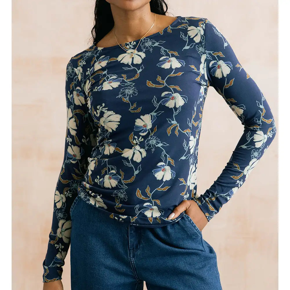A woman wearing a navy blue long-sleeve top with a white and light blue floral print, paired with blue jeans, against a soft beige background.