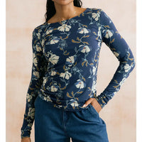 A woman wearing a navy blue long-sleeve top with a white and light blue floral print, paired with blue jeans, against a soft beige background.
