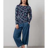 Woman wearing a navy floral top and blue jeans against a plain background