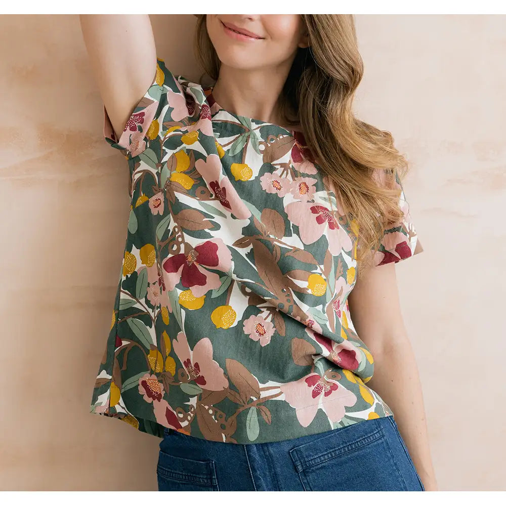 Sage green top with floral design on it in browns, pinks and yellows. Short sleeves and round neckline. 