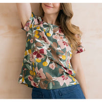 Sage green top with floral design on it in browns, pinks and yellows. Short sleeves and round neckline. 