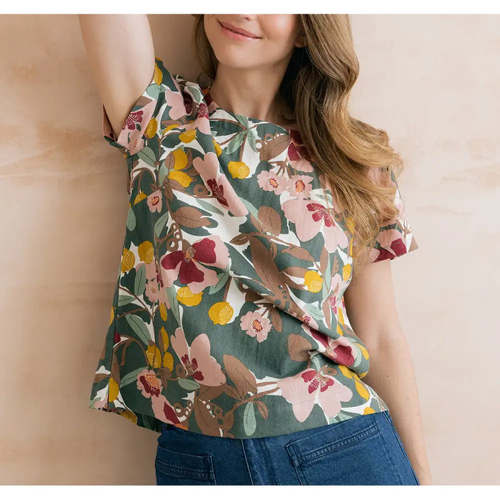 Sage green top with floral design on it in browns, pinks and yellows. Short sleeves and round neckline. 