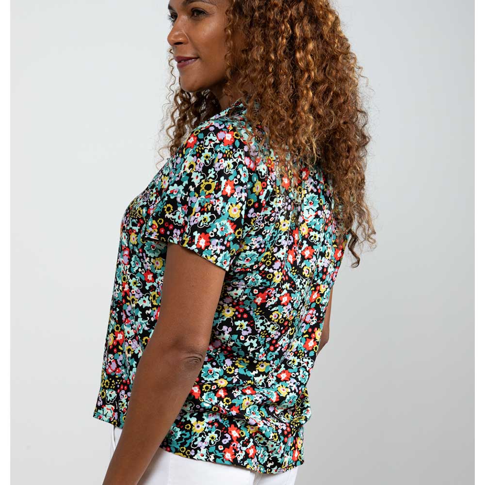 Model with brown wavy hair wearing a black floral print shirt with short sleeves - angle from the side