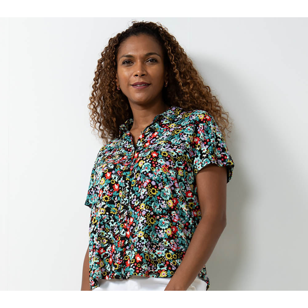 Brown curly haired model in a floral print shirt with short sleeves and collar