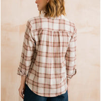 A woman shown from the back wearing a cream-colored plaid button-up shirt with red and brown lines, paired with dark blue jeans, against a textured beige wall.