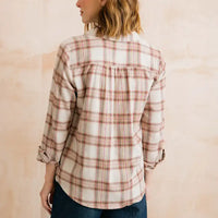 A woman shown from the back wearing a cream-colored plaid flannel shirt with red and brown lines, paired with dark blue jeans, against a soft beige textured wall.
