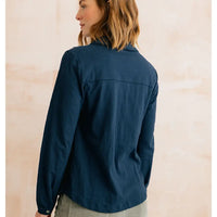 A woman shown from the back wearing a dark navy blue long-sleeve button-up shirt against a light beige textured wall.