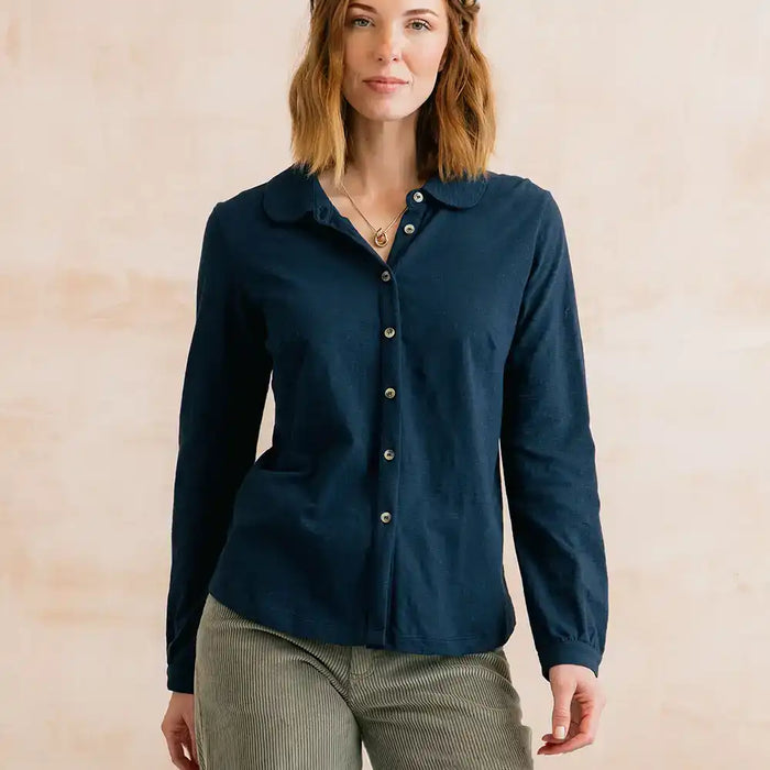A woman wearing a dark navy blue long-sleeve button-up shirt with a collar, paired with olive green corduroy pants, standing against a neutral beige background.
