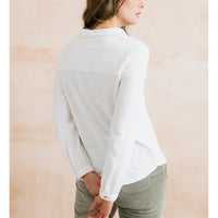 A woman shown from the back wearing a white long-sleeve collared shirt and light olive green corduroy pants, set against a soft beige textured background.