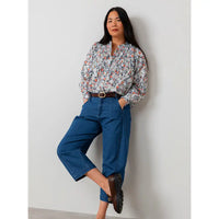 Woman wearing a floral blouse and blue jeans against a white wall