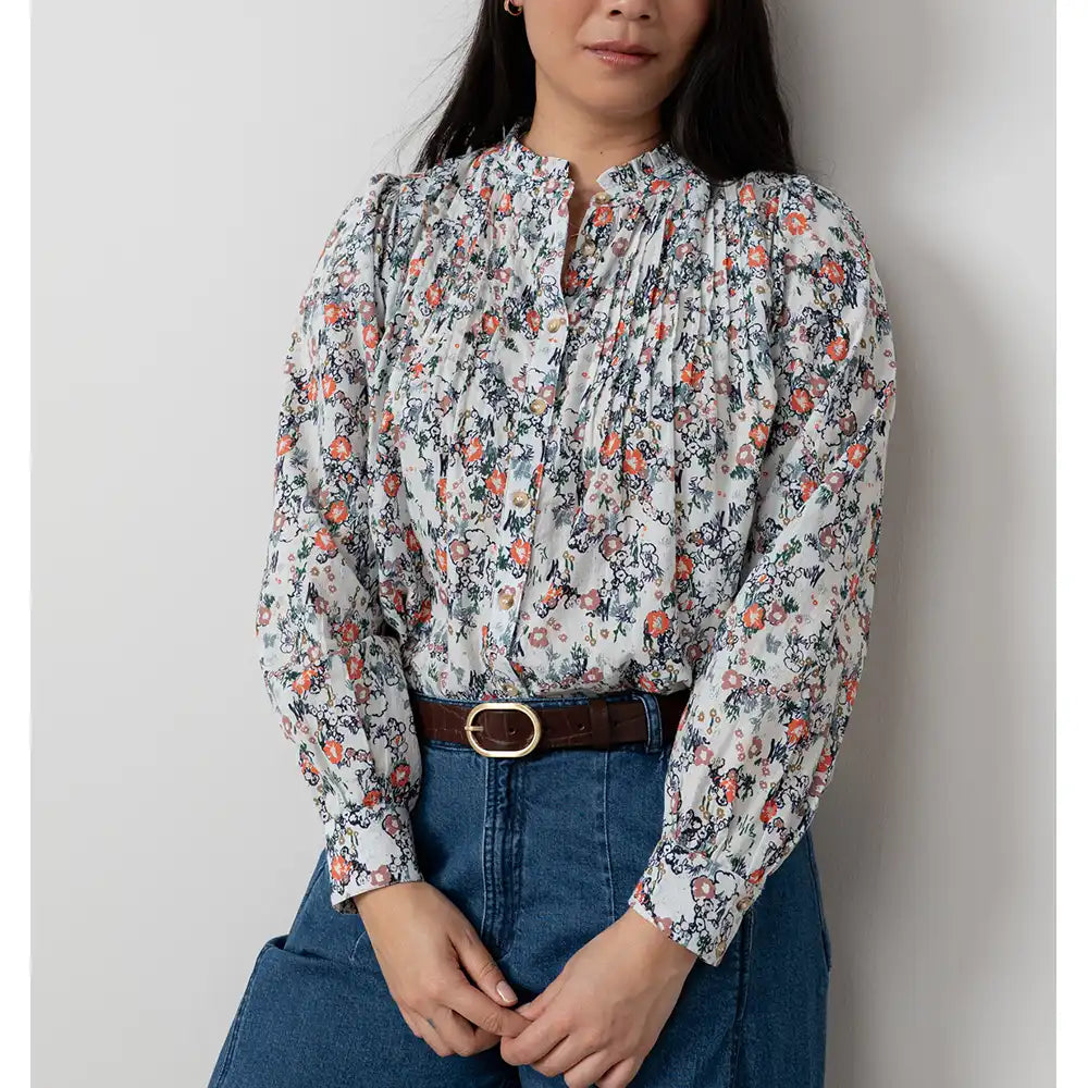 Woman wearing a floral blouse and blue jeans against a plain background