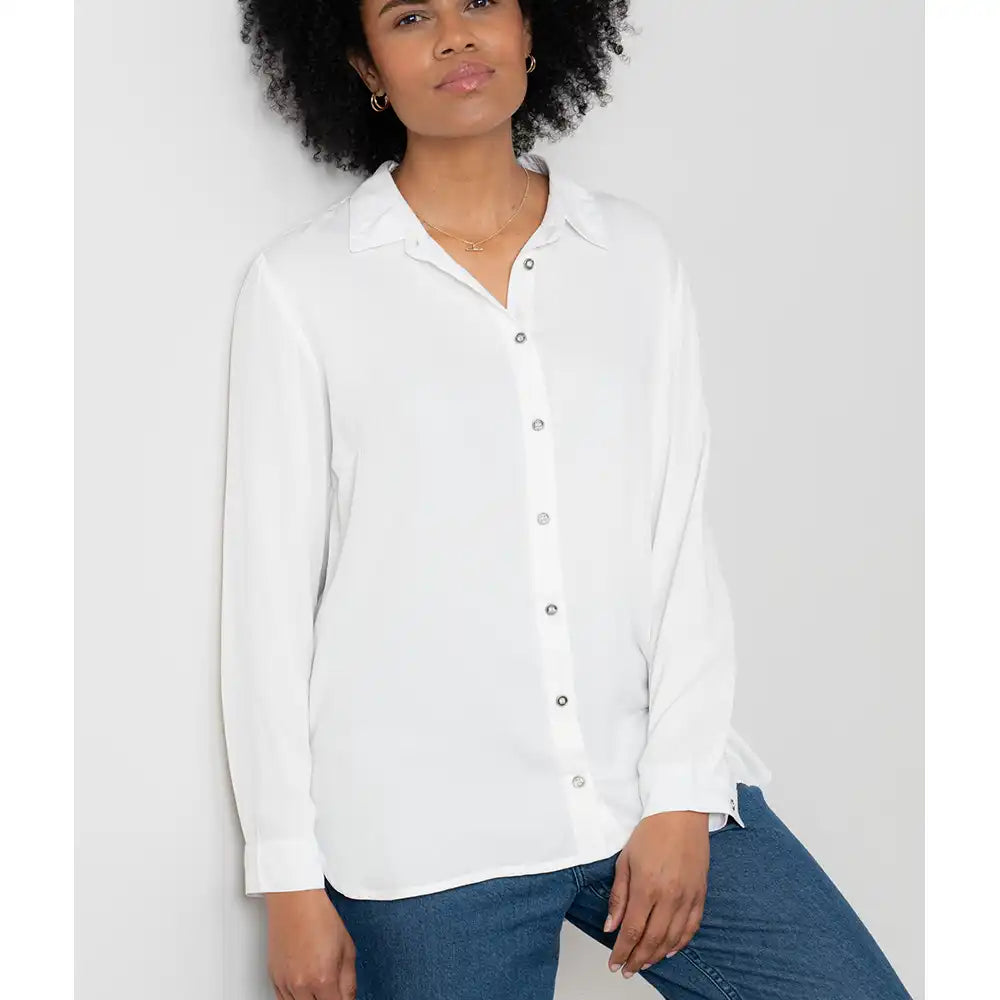 Woman wearing a white button-up shirt and blue jeans against a plain background
