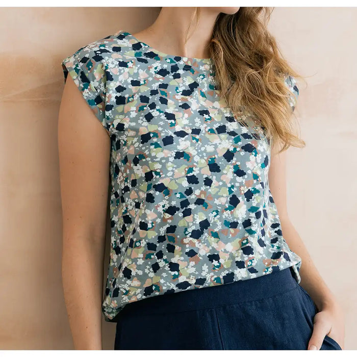 Front of a pale blue top with mottled design. Design has navy, white, pale pink and teal. Short sleeves and round neck.