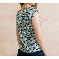 Side of a pale blue top with mottled design. Design has navy, white, pale pink and teal. Short sleeves and round neck.