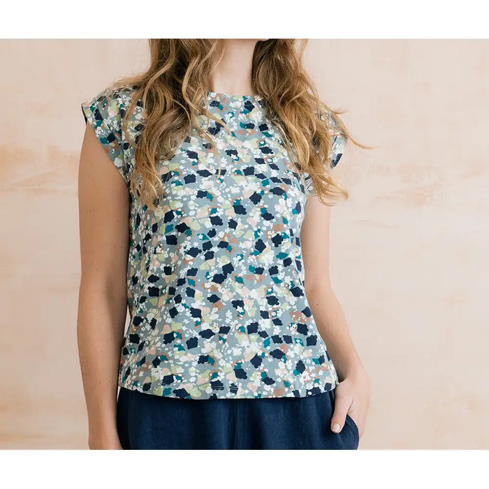 Front of a pale blue top with mottled design. Design has navy, white, pale pink and teal. Short sleeves and round neck.