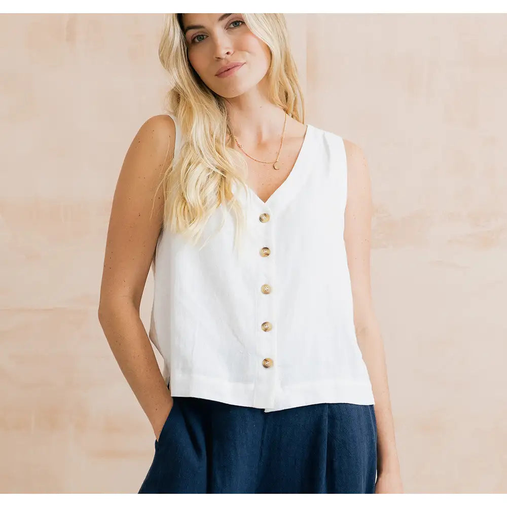 Woman wearing a white sleeveless button-up top with a beige background