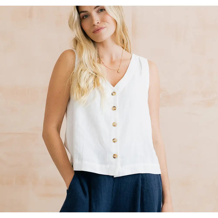 Woman wearing a white sleeveless button-up top with a beige background