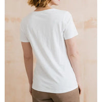 Person wearing a plain white t-shirt against a light wooden background