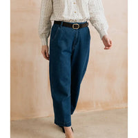 A person wearing dark blue wide-leg cropped jeans with a black belt, paired with a cream striped long-sleeve blouse, standing against a textured beige wall.