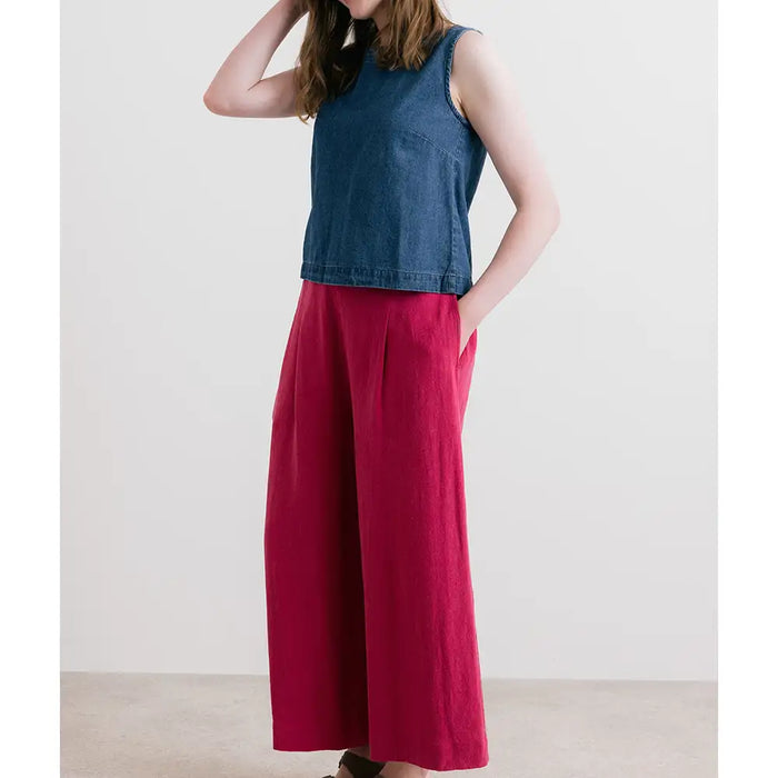 Person wearing a blue sleeveless top and red wide-leg pants against a white background