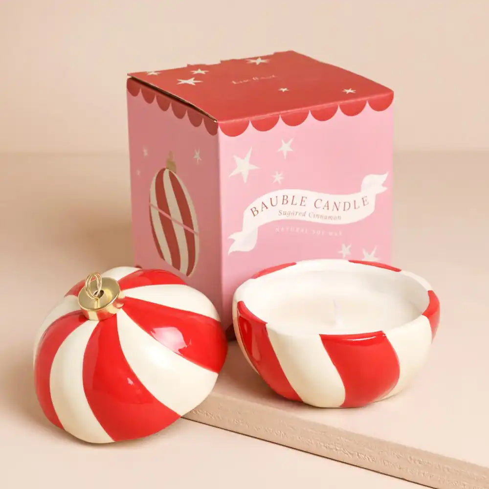 A scented bauble candle set with a red and white striped spherical lid and matching bowl, shown next to its pink packaging box.